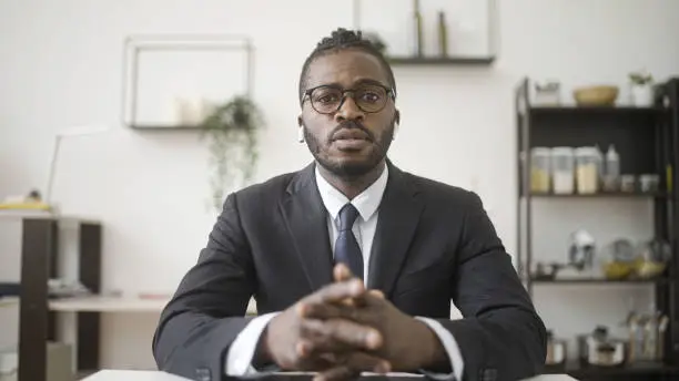 Afro-american businessman in suit having online call, hearing bad news, distance work