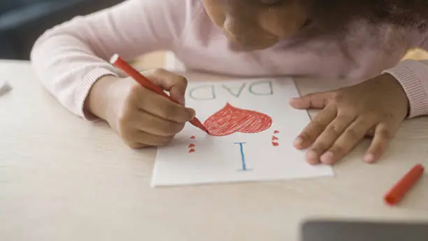 Young girl with afro hair drawing greeting card for father's day, daughters love