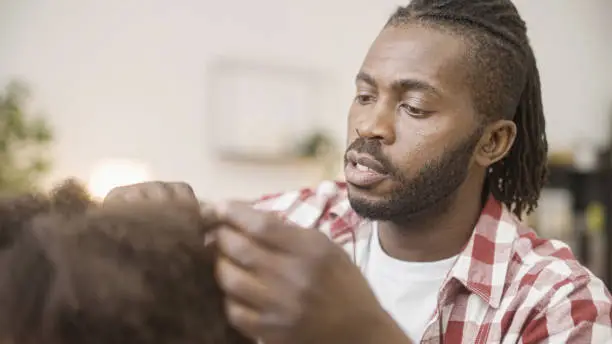 Confused african father trying to comb unruly curly hair of little daughter