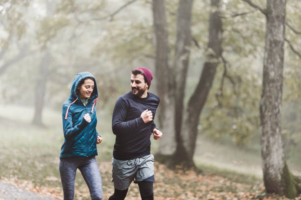 istock Happy athletic couple talking while running during cold day in misty forest. 1341439553