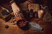 Female witch making potion on dark background, magic bottles with potions and candles on table of alchemist, Halloween theme