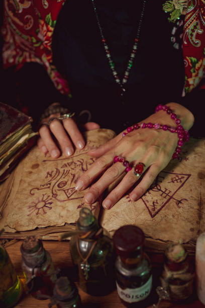 istock Female witch making potion on dark background, magic bottles with potions and candles on table of alchemist, Halloween theme 1341442894