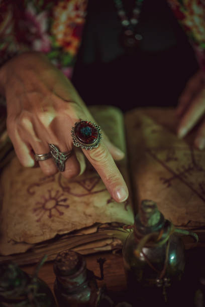 istock Female witch making potion on dark background, magic bottles with potions and candles on table of alchemist, Halloween theme 1341443723