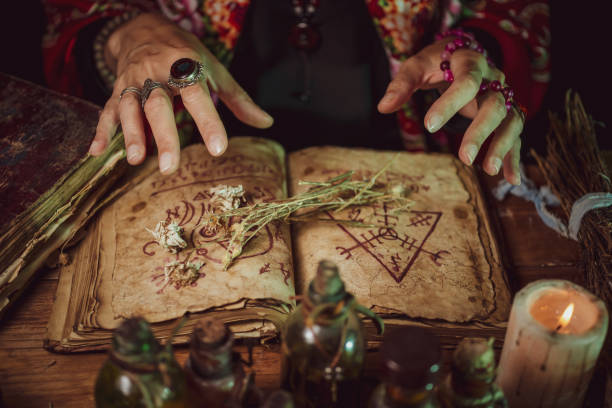istock Female witch making potion on dark background, magic bottles with potions and candles on table of alchemist, Halloween theme 1341443753