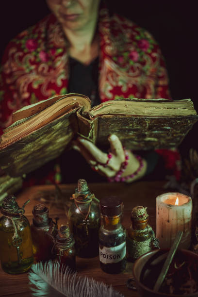 istock Female witch making potion on dark background, magic bottles with potions and candles on table of alchemist, Halloween theme 1341444270
