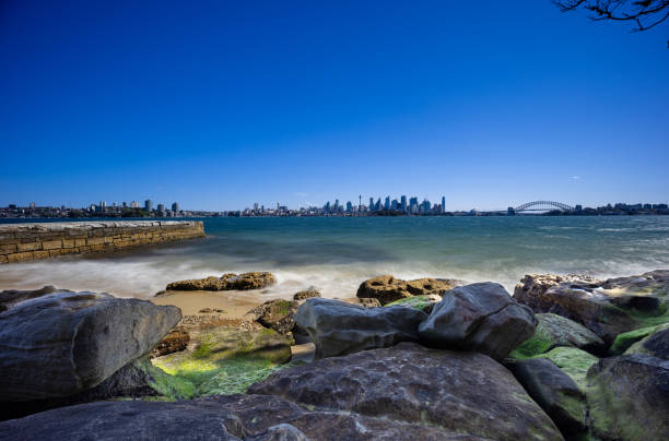 istock Sunny Spring day on Sydney Harbour with nice rocks in the foreground the soft waves crashing on the shore and the beautiful harbour foreshore as a backdrop NSW Australia 1341446525