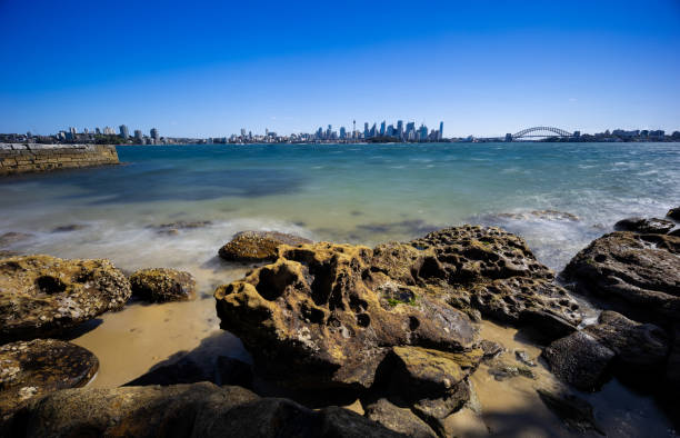 istock Sunny Spring day on Sydney Harbour with nice rocks in the foreground the soft waves crashing on the shore and the beautiful harbour foreshore as a backdrop NSW Australia 1341446526