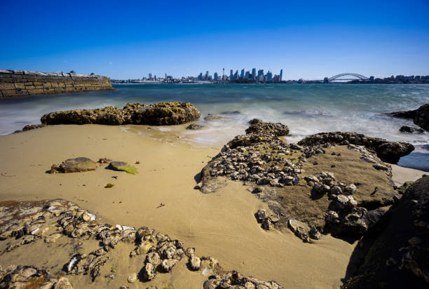 Sunny Spring day on Sydney Harbour with nice rocks in the foreground the soft waves crashing on the shore and the beautiful harbour foreshore as a backdrop NSW Australia