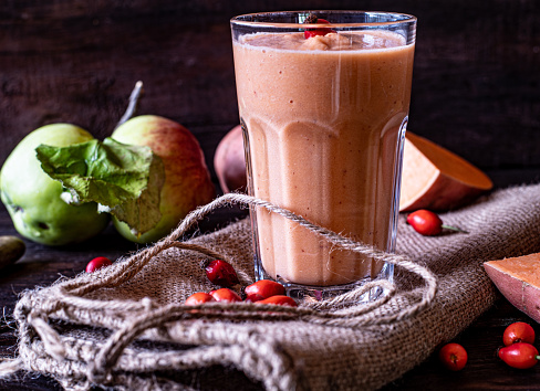Delicious smoothie with sweet potatoes and wild fruits such as wild apples and rose hips served in a rustic glass on wooden table. Closeup view with blurred background