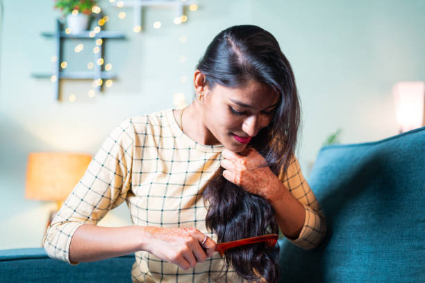 Young Indian girl on sofa combing her long hairs - concept of woman getting ready and daily rituals. Young Indian girl on sofa combing her long hairs - concept of woman getting ready and daily rituals asian bruhing hair stock pictures, royalty-free photos & images