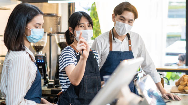 istock Asian coffeehouse worker people meeting and discuss work plan in store. attractive Cafe business manager leader wear mask due to Covid19, explain job work to barista and waitress to reopen restaurant. 1341450502