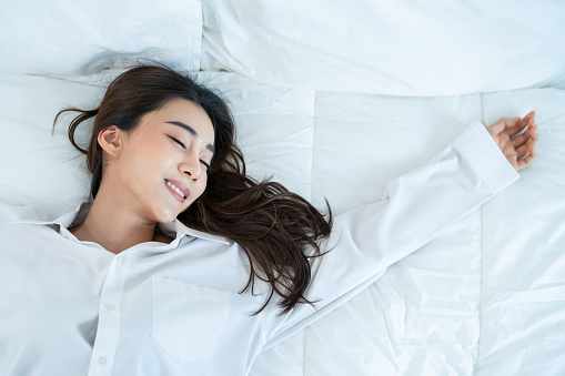 Asian beautiful comfort girl in pajamas get up from sleep in bedroom. Attractive young woman lying down on bed feel happy with cozy pillow and blanket enjoy early morning after wake up in room at home