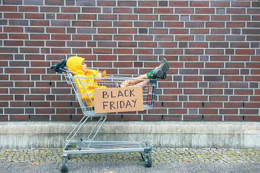 Girl in yellow jacket sitting relaxed inside the shopping cart with a black friday sign
