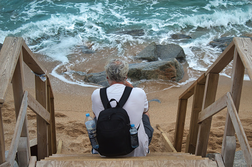 hombre maduro sentado en una escalera de madera junto al mar en una playa de Vilassar de Mar, España photo
