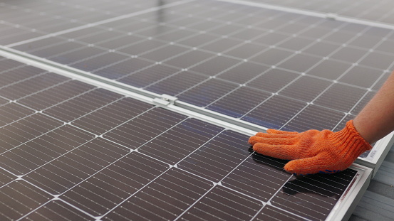 Unrecognizable man glove wiping solar panel from dust on sunny day. Close up of a young engineer hand is checking the operation of sun and cleanliness of photovoltaic solar panels on a sunset
