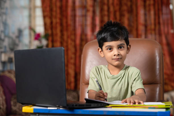 маленький мальчик, посещающий занятия онлайн-школы с использованием ноутбука дома. - reading and writing little boys reading asian ethnicity стоковые фото и изображения