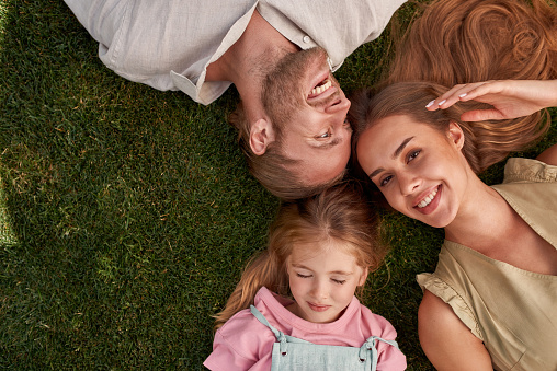 Top view of happy young parents with little daughter lying on green grass in summer park. Childhood, parenting, relax concept