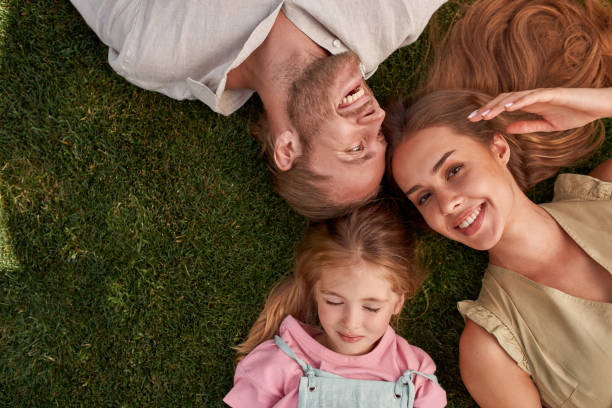 Top view of happy young parents with little daughter lying on green grass in summer park stock photo