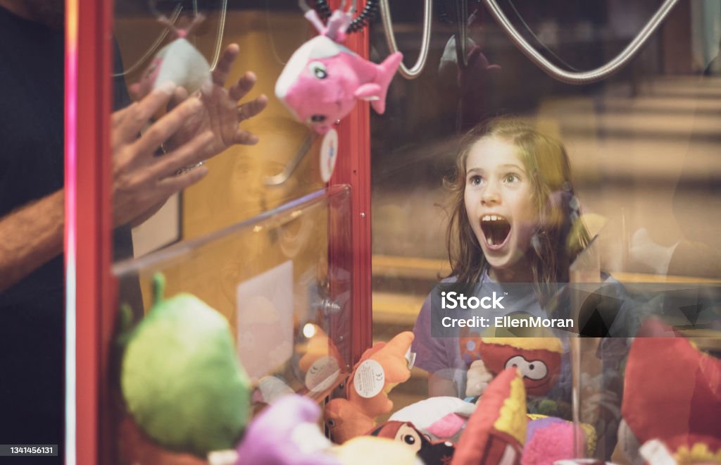 Arcade Fun A little girl is excited as she watches her father win a prize from an arcade machine. Toy Grabbing Game Stock Photo