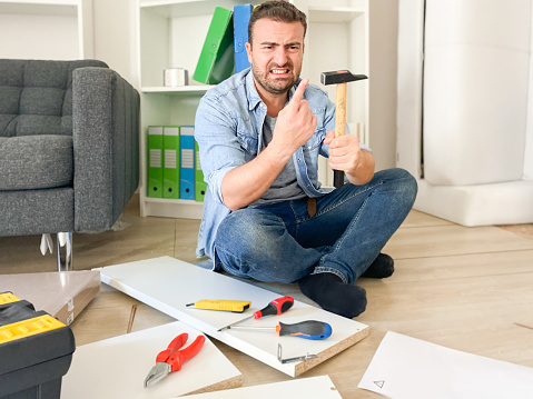 One man hitting his thumb with the hammer assembling furniture part