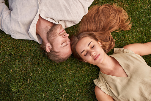 Top view of relaxed young couple lying together on green grass with eyes closed. Relationships concept