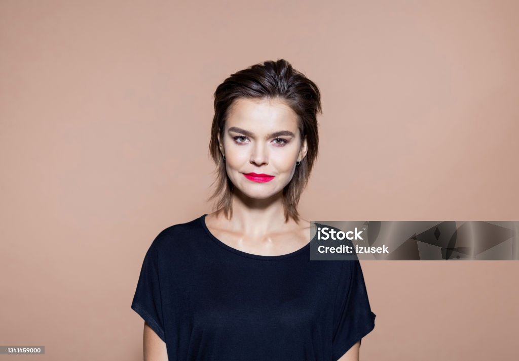 Businesswoman standing against brown background Portrait of entrepreneur with black short hair. Serious businesswoman standing against brown background, smiling at camera. She wearing black blouse. Design Professional Stock Photo