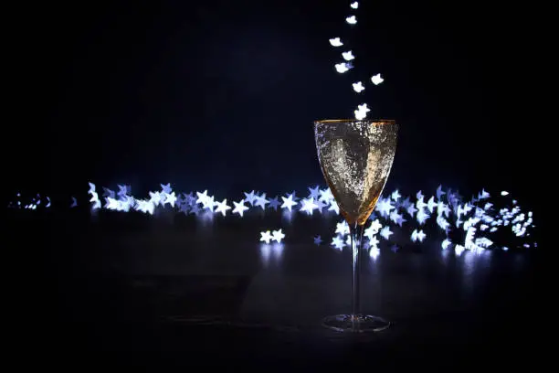 Golden festive glass on a dark background and magic bokeh in the form of stars pouring into the glass. Christmas background, place for text.
