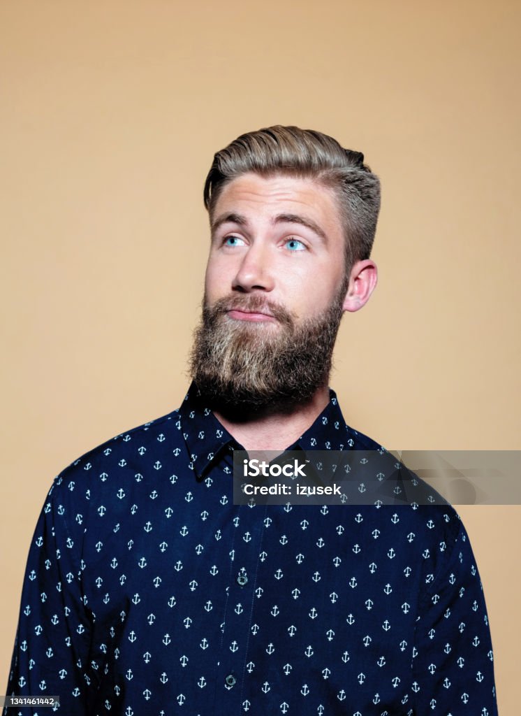 Headshot of surprised bearded young man Portrait of thoughtful entrepreneur. Bearded young businessman standing against brown background, looking away. He is in casuals. Problems Stock Photo