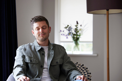 Peaceful Man Meditating Sitting In Chair At Home