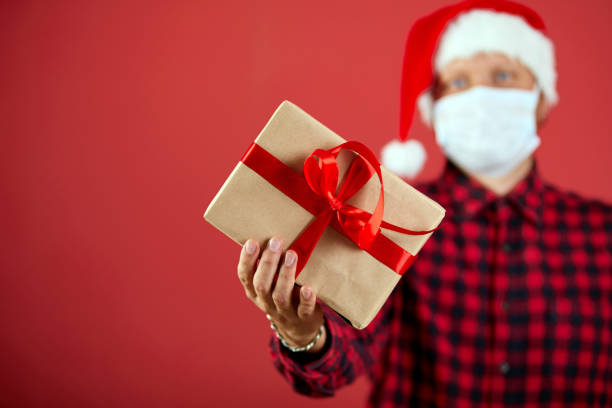 istock Man in protective face mask and Santa hat with Christmas DIY gift 1341461881