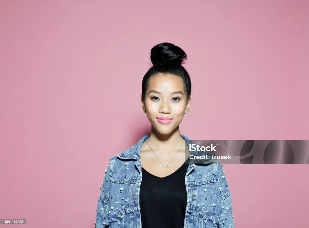 Smiling young woman against pink background Portrait of confident asian young woman. Female entrepreneur wearing oversized denim jacket standing against pink background, looking at camera. Only Women Stock Photo
