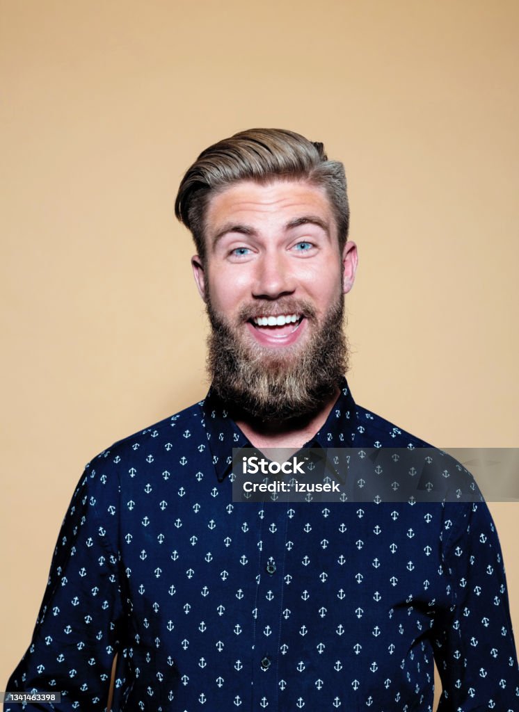 Surprised young man standing over brown background Portrait of happy entrepreneur. Bearded young businessman with toothy smile standing against brown background. He is in casuals. Surprise Stock Photo