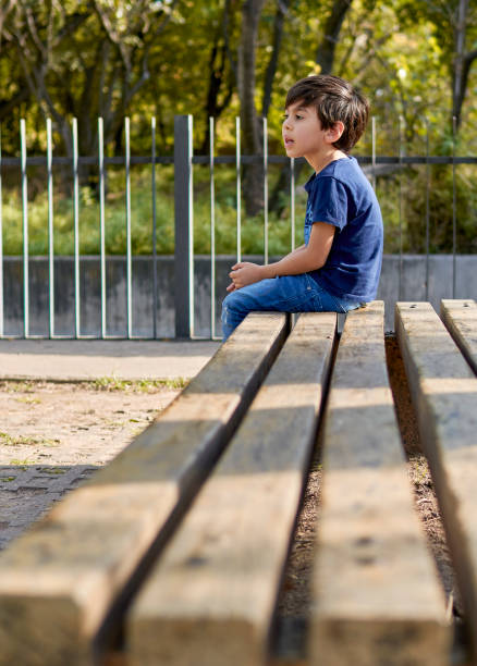 latin boy sitting in profile waiting on a square bench. vertical
