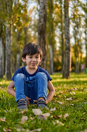Latin kid displeased with a blank stare sitting in forest in autumn time. vertical, copy space and blurred background
