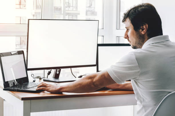 istock Man at workplace with two laptops and monitor 1341465322