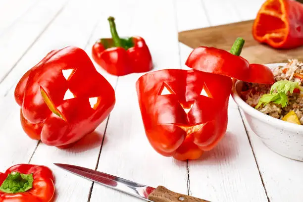 Halloween fest food idea Jack-o'-Pepper. Red peppers carved like Jack-o'-lanterns ready to stuffed with rice and meat, or legumes.
