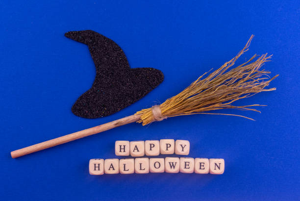 Black witch hat, broom and happy halloween  lettering on blue background.