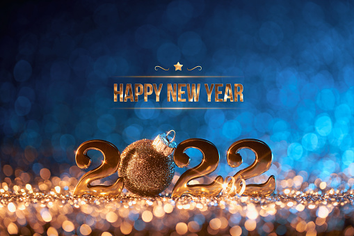 Abstract Christmas / New Year 2022 background. Golden serif numbers and a black glitter Christmas ornament on shiny stars, glitter and defocused lights in a yellow blue contrast.