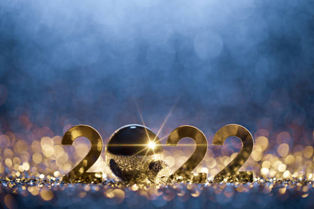Abstract Christmas / New Year 2022 background. Metallic numbers and a Christmas ornament on shiny stars, glitter and defocused lights in a yellow blue contrast.