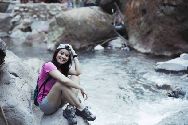 istock woman, with backpack walking on rocks to cross a river during a summer day 1341469516