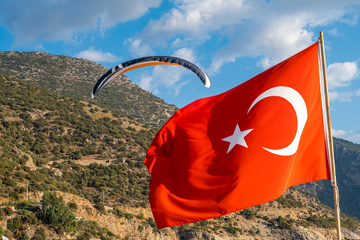 Paragliding is about to land behind the Turkish flag waving at sunset