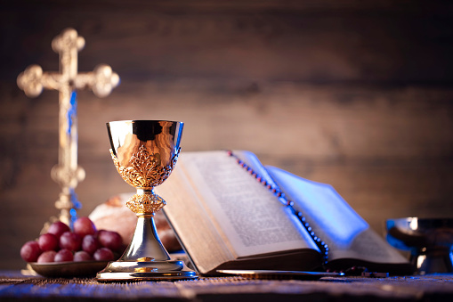 Catholic symbols composition. The Cross, Holy Bible, rosary and golden chalice on the altar.