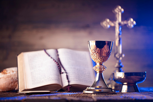 Catholic symbols composition. The Cross, Holy Bible, rosary and golden chalice on the altar.