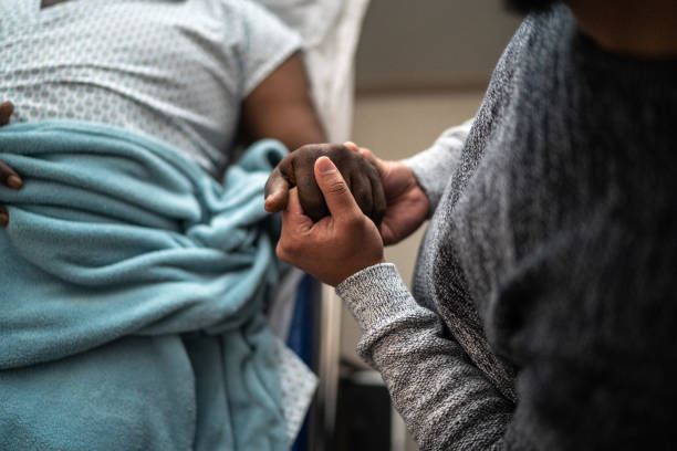 sohn hält vaters hand im krankenhaus - bett stock-fotos und bilder