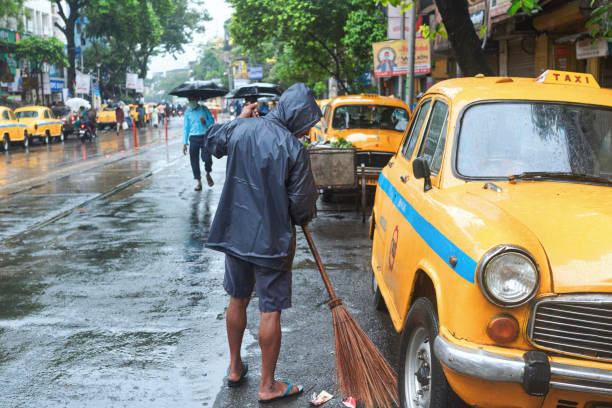 ein reinigungspersonal, das nach einem sintflutartigen regen müll aus der mitte der straße entfernt - drenched raincoat rain clothing stock-fotos und bilder