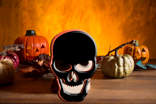 Bright orange background appears as to be an inferno with Halloween decorations in foreground.  Pirate head in foreground.  Skull in foreground.