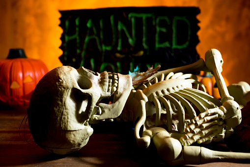 Bright orange background appears as to be an inferno with Halloween decorations in foreground.  Pirate head in foreground.  Skeleton lying down in foreground.