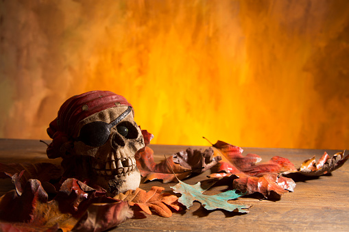Bright orange background appears as to be an inferno with Halloween decorations in foreground.  Pirate head in foreground.  Pirate Skull in foreground.