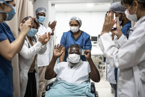 doctors and nurses celebrating senior man leaving the hospital after recovery - wearing protective face mask - ziekenhuis stockfoto's en -beelden