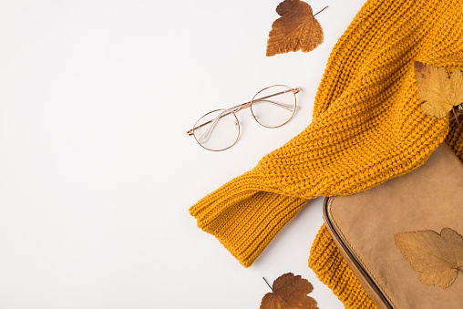 Top view photo of orange sweater glasses leather bag and yellow autumn leaves on isolated white background with empty space